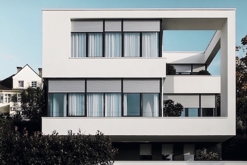 Weißes modernes kastenförmiges Haus mit grauen Fenstern und Rollläden