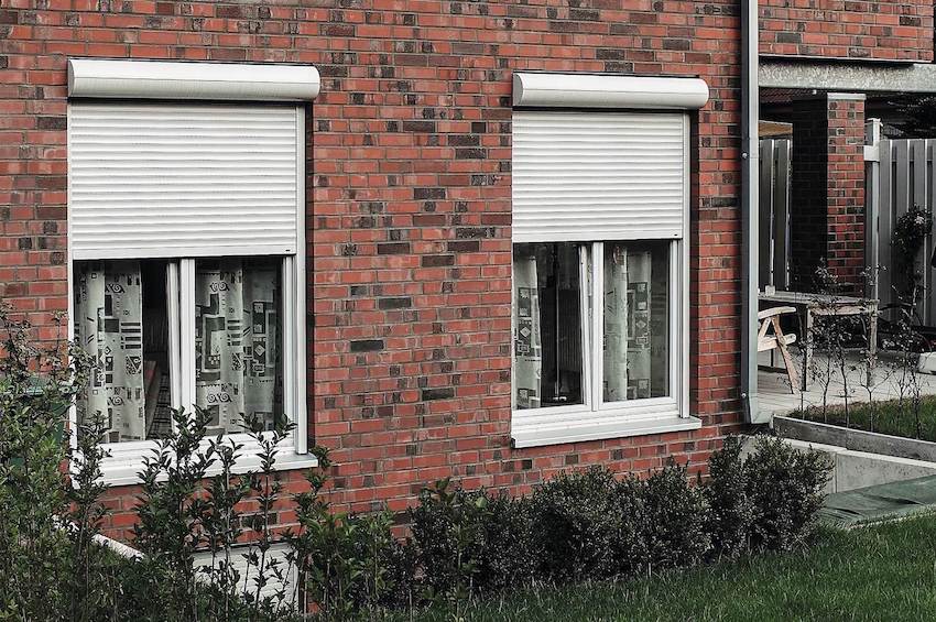 Klinker_klein Weißes modernes kastenförmiges Haus mit grauen Fenstern und Rollläden