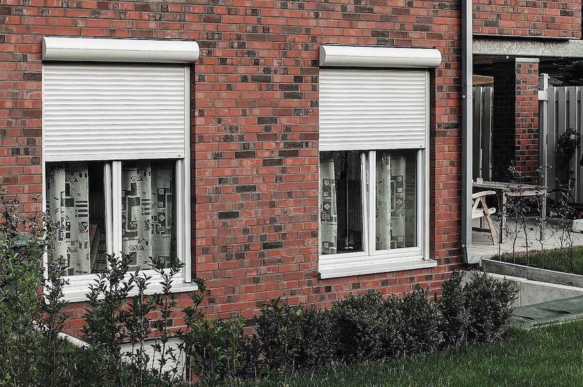 Weißes modernes kastenförmiges Haus mit grauen Fenstern und Rollläden